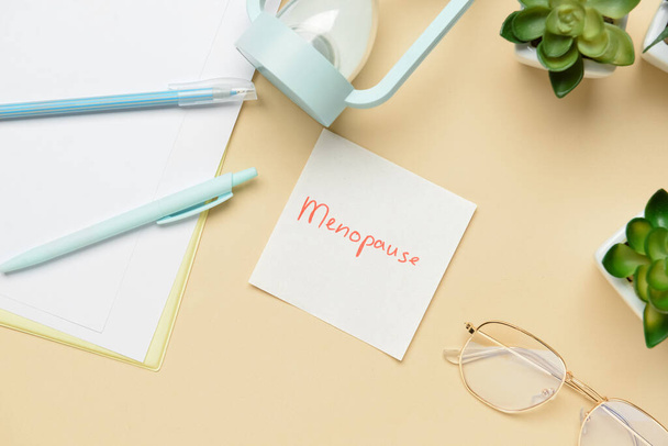 Nota adesiva con la parola MENOPAUSA, occhiali e penne su sfondo beige - Foto, immagini