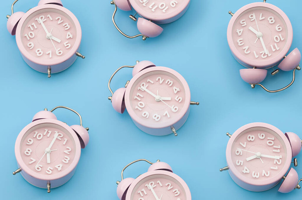 Nostalgia repetitive wallpaper and passing of time concert with minimalist seamless pattern layout of pastel pink mechanical alarm clock isolated on vibrant blue background - Photo, image