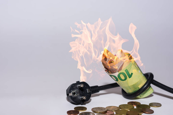 Energiepreise steigen und Energieverbrauch Stromkabel mit brennenden Euroscheinen und Münzen mit grauem Hintergrund - Foto, Bild