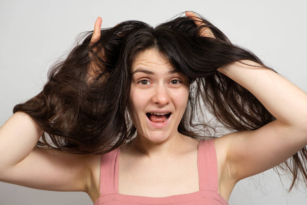 Eine schöne brünette Frau mit langen Haaren auf weißem Hintergrund hält ihre Hände auf dem Kopf und denkt darüber nach, was für eine Frisur zu tun ist - Foto, Bild