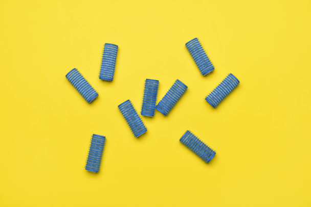 Blue hair curlers on yellow background - 写真・画像