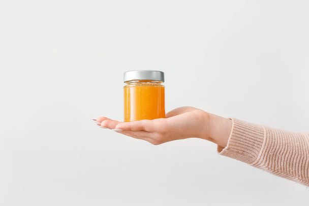 Female hand with jar of tasty orange jam on light background - Photo, image