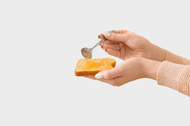 Donna che diffonde gustosa marmellata di arance sul pane tostato su sfondo chiaro - Foto, immagini