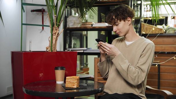 Крупный план парня, сидящего в кафе и фотографирующего композицию на столе со своим телефоном. Кофейня - Фото, изображение