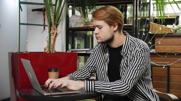 Közelkép egy fickóról, aki egy kávézóban ül egy laptoppal az asztalnál, kávét iszik és videokapcsolaton keresztül beszél. Otthonon kívül dolgozni. - Fotó, kép