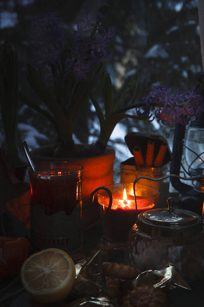Still life with a cup of tea, burning candle and hyacinth flowers in pots in front of frozen winter window, cozy evening concept. - 写真・画像