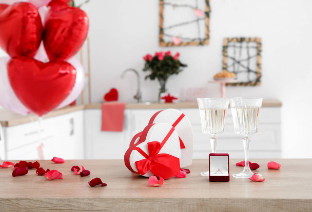 Glas champagne, geschenkdozen en verlovingsring op tafel in de keuken - Foto, afbeelding