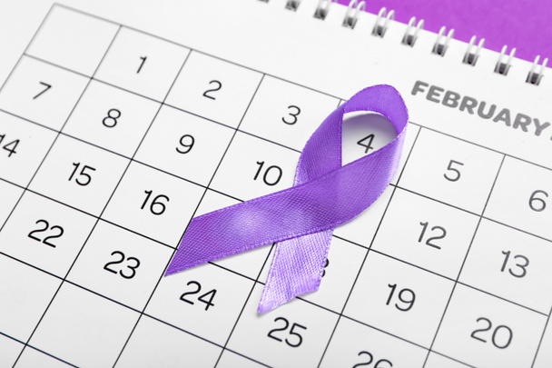 Awareness ribbon and paper calendar with marked date of World Cancer Day on color background, closeup - Photo, Image