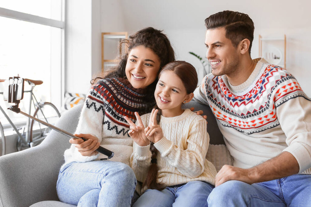 Boldog szülők kislányukkal meleg pulóverben, akik otthon szelfit készítenek. - Fotó, kép
