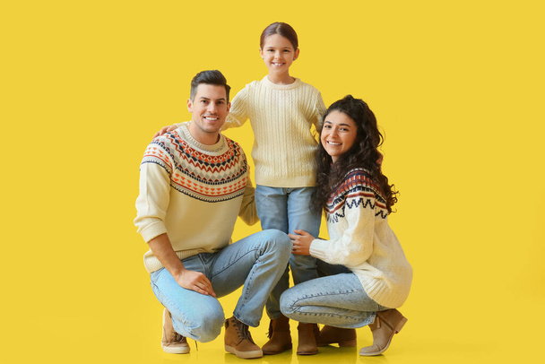 Onnelliset vanhemmat, joilla on pieni tytär lämpimissä villapaidoissa keltaisella taustalla - Valokuva, kuva
