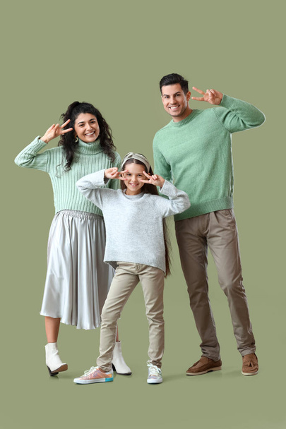 Happy family in warm sweaters showing victory gesture on green background - Photo, Image