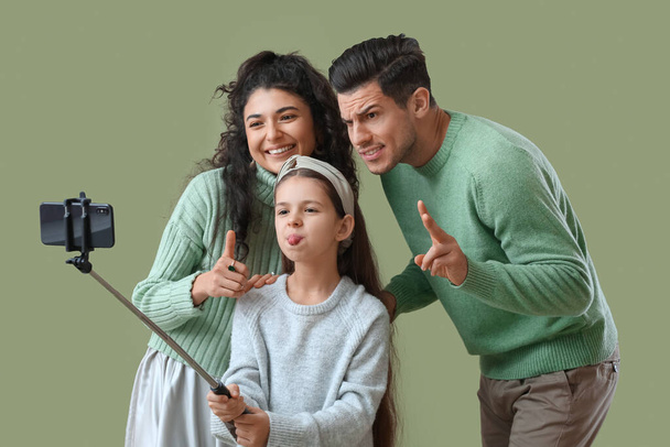 Gelukkig ouders met kleine dochter in warme truien nemen selfie op groene achtergrond - Foto, afbeelding