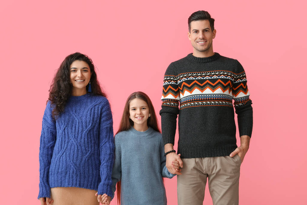 Kleines Mädchen und ihre Eltern in warmen Pullovern halten Händchen auf rosa Hintergrund - Foto, Bild