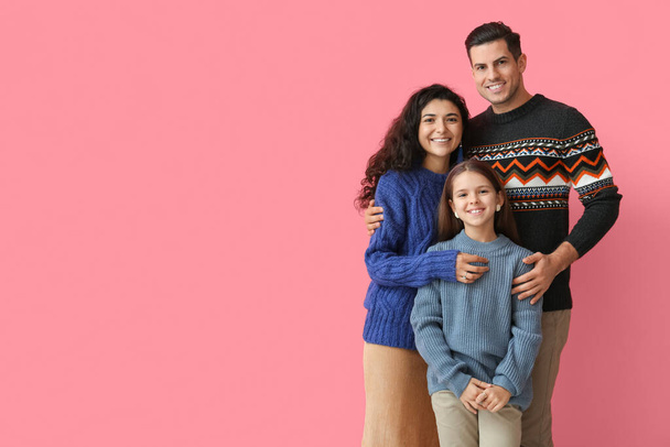 Little girl with her parents in warm sweaters hugging on pink background - Photo, Image