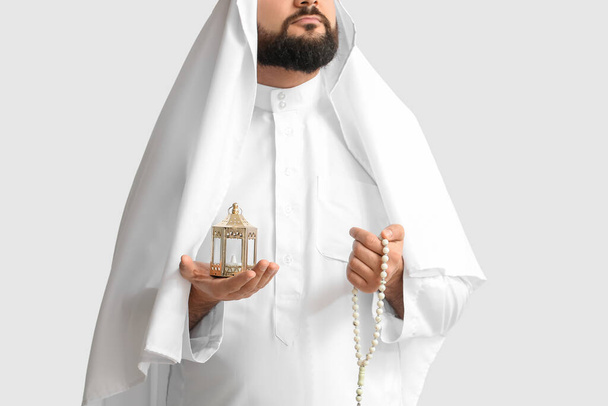 Muslim man with prayer beads and lamp on light background - Foto, afbeelding