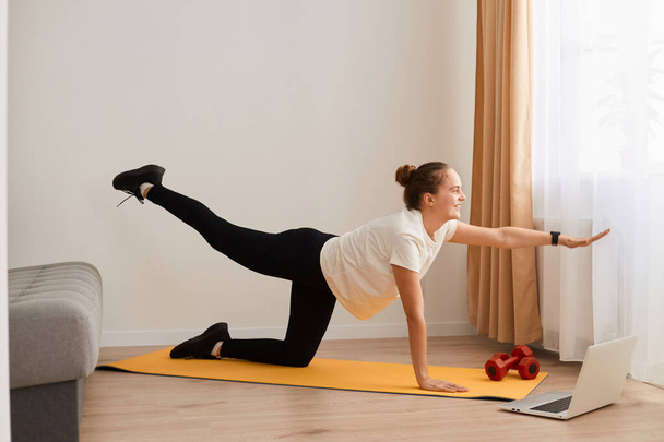Caucasian athletic woman wearing sportswear standing in plank pose with arm leg lifted up, doing yoga fitness training workout at home, stretching core exercise on mat on floor. - Φωτογραφία, εικόνα