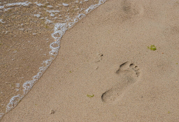 Fußabdrücke eines Mannes am gelben Strand Sand vom Barfußlaufen am Meer mit Wasser, das die Fußabdrücke wegspült. Kontemplation des Lebens - Foto, Bild