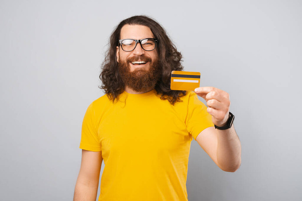 Szczęśliwy młody człowiek z brodą i długimi włosami pokazując żółte puste karty kredytowe - Zdjęcie, obraz