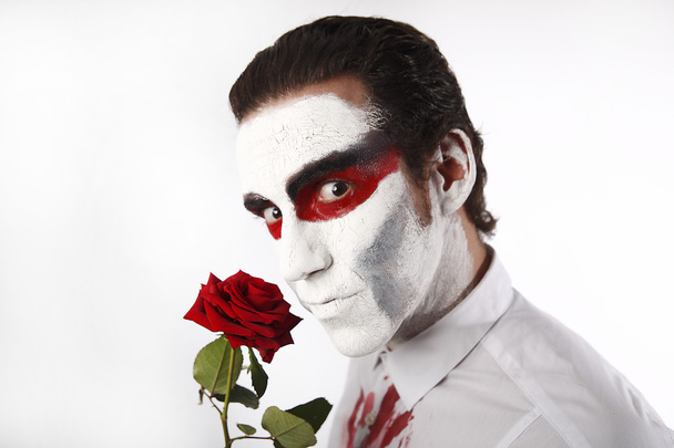 man met witte mascara en bloedige shirt bezit rode rose - Foto, afbeelding