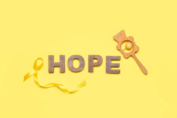 Złota wstążka świadomości, grzechotka i słowo HOPE na żółtym tle. Międzynarodowy Dzień Raka Dzieciństwa - Zdjęcie, obraz