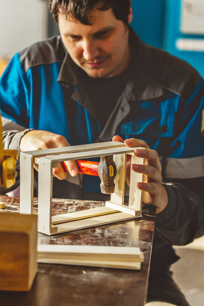 Молодий кавказький тесляр у робочому одязі виготовляє дерев'яні коробки в теслярській майстерні. Справжня сцена. Маленький бізнес - Фото, зображення