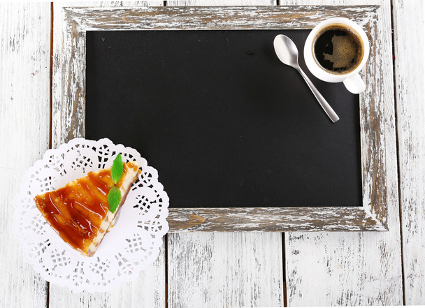 Cheese cake on paper napkin and cup of coffee on blackboard on wooden background - Foto, immagini
