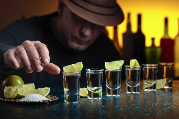 L'homme au chapeau boit de la tequila avec du sel et des tranches de citron vert. Concentration sélective. - Photo, image