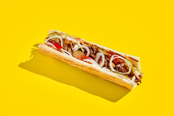 Beef cheesesteak with onion and pickle in minimal style. American fast food in yellow background with shadow. Philly steak sandwich trendy concept. Junk food in colour background - Foto, immagini