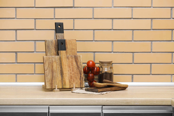 Drewniane deski, łyżki i kosz z pomidorami na stole przy ścianie z cegły - Zdjęcie, obraz