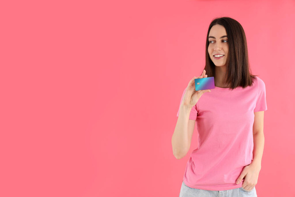 Vonzó nő pólóban tartja kártya rózsaszín háttér - Fotó, kép