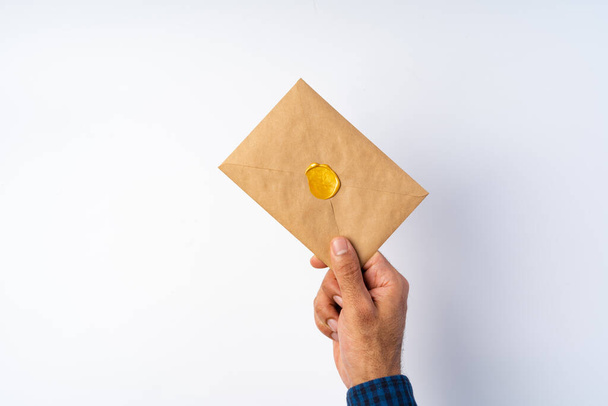Male hand holding closed envelope above the white surface - Foto, afbeelding