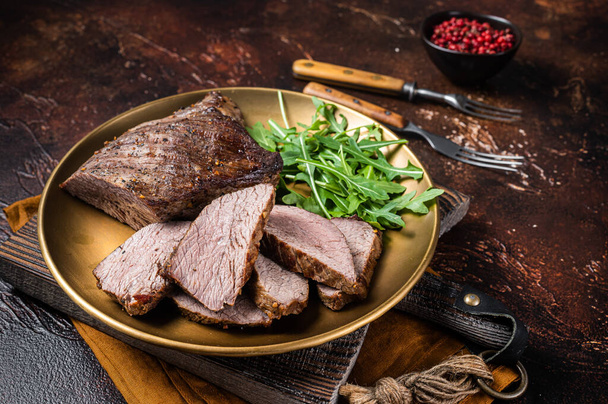 Pörkölt Tri Tip vagy hátszín marhahús steak egy tányéron rukkolával. Sötét háttér. Felülnézet - Fotó, kép