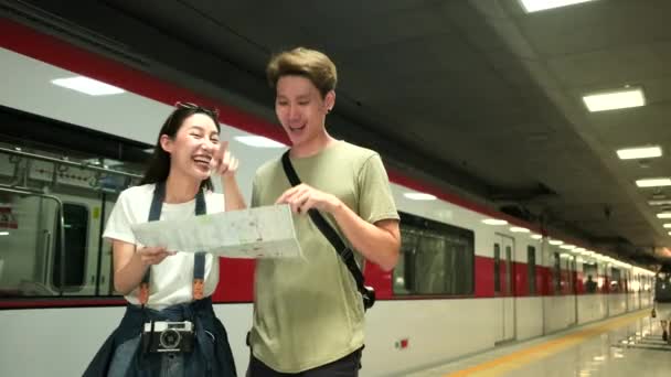 Thai man helps beautiful Asian female tourist search information and find location for travel at public train station platform, passenger trip lifestyle, casual transportation in journey vacation.  - Imágenes, Vídeo