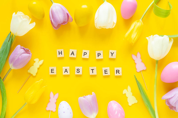 Greeting card with text HAPPY EASTER. Multicolored easter eggs and tulips on yellow background - Photo, Image