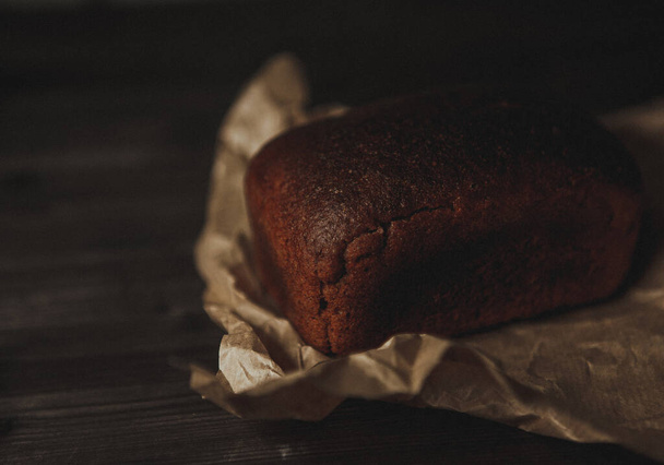 freshly baked black rye bread on a dark background and on craft paper. Dark moody background with free text space. top view - Fotó, kép