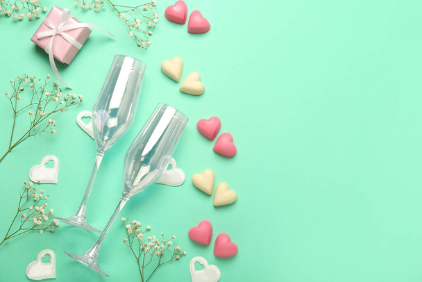 Composition with tasty heart-shaped candies, glasses and flowers for Valentine's Day celebration on turquoise background - Photo, Image