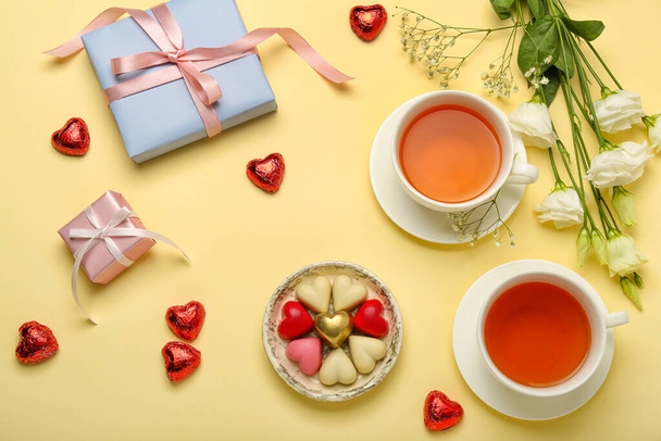 Kompozycja ze smacznymi cukierkami w kształcie serca, kwiatami i filiżankami herbaty na Walentynki na beżowym tle - Zdjęcie, obraz