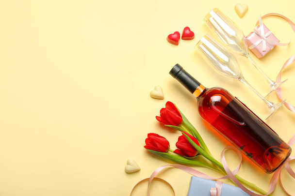 Σύνθεση με νόστιμες καραμέλες σε σχήμα καρδιάς, μπουκάλι κρασί και λουλούδια για τον εορτασμό της ημέρας του Αγίου Βαλεντίνου σε μπεζ φόντο - Φωτογραφία, εικόνα