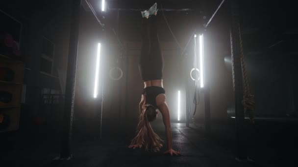 A strong young athletic woman goes upside down on her hands in the gym. A woman is fit on her hands in a dark gym. Training at least upside down - Footage, Video