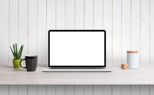Lapop on desk with isolated white screen for mockup, app or web page design promotion. White wooden wall in background - Fotografie, Obrázek