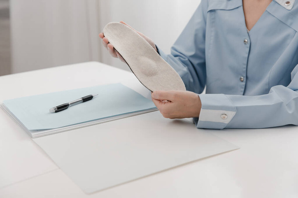Doctor holding an insole while sitting at a table. Orthopedist tests the medical device. Orthopedic insoles. Foot care. Flat Feet Correction. Treatment and prevention of flat feet and foot diseases - Φωτογραφία, εικόνα