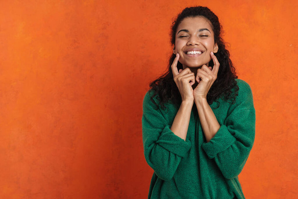 Happy smiling african casual brunette woman standing over orange wall background, grimacing, touching face - Photo, image