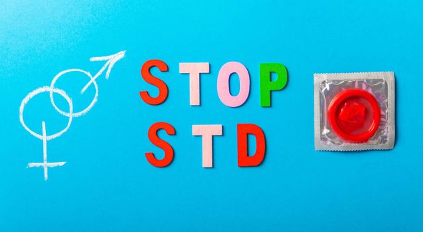 Colorful blocks with "STOP STD" phrase background, flat lay. Super safe strawberry condoms with a pleasant smell on a blue background. Contraceptives are made from natural rubber latex, high - Foto, afbeelding