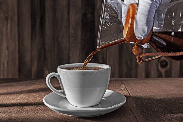 Hand Weared In White Glove Pours Fresh Brewed Tasty Coffee From Coffee Dripper Into Ceramic Cup - Fotó, kép