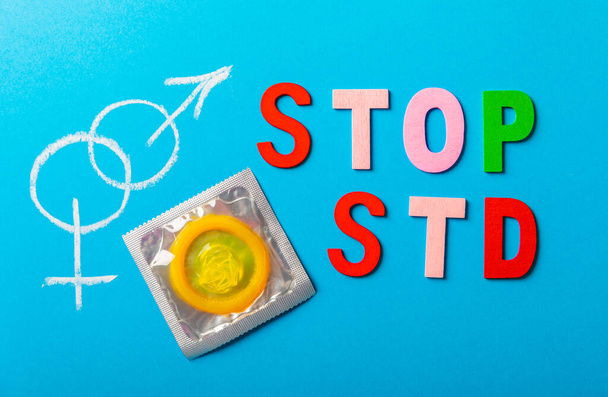 Colorful blocks with "STOP STD" phrase background, flat lay. Super safe strawberry condoms with a pleasant smell on a blue background. Contraceptives are made from natural rubber latex, high - Photo, Image