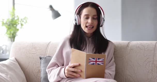 Kobieta w słuchawkach studiuje angielski w domu 4k film - Materiał filmowy, wideo