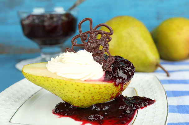 Tasty dessert with pear, cream and berry sauce on plate, on color wooden background - Foto, imagen