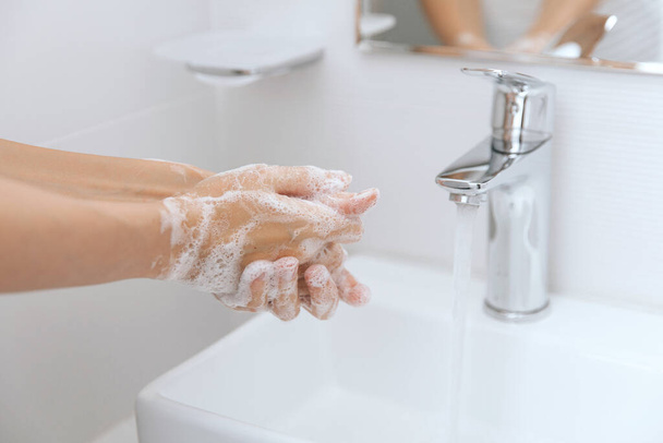 Washing hands under the flowing water tap. Hygiene concept hand detail. Washing hands rubbing with soap for corona virus prevention, hygiene to stop spreading corona virus in or public wash room - 写真・画像