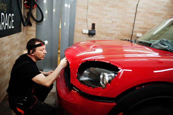 Car service worker put anti gravel film on a red car body at the detailing vehicle workshop. Car protection with special films. - Fotografie, Obrázek