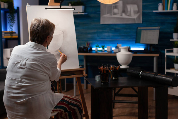Starsza kobieta cieniowanie szkic w studium światła w klasie wieczorem uczucie inspiracji rysunek martwa natura wazon tryb - Zdjęcie, obraz